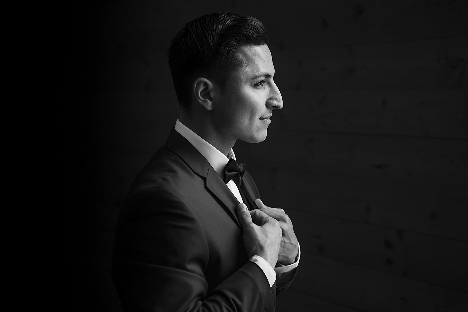 A man in a tuxedo and bow tie is adjusting his tie.