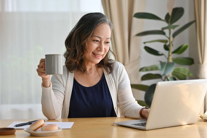 Woman smiling on a video call holding a cup of coffee.