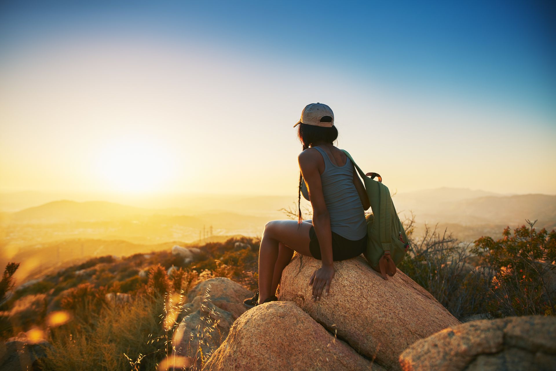 A woman is sitting on top of a rock looking at the sunset.