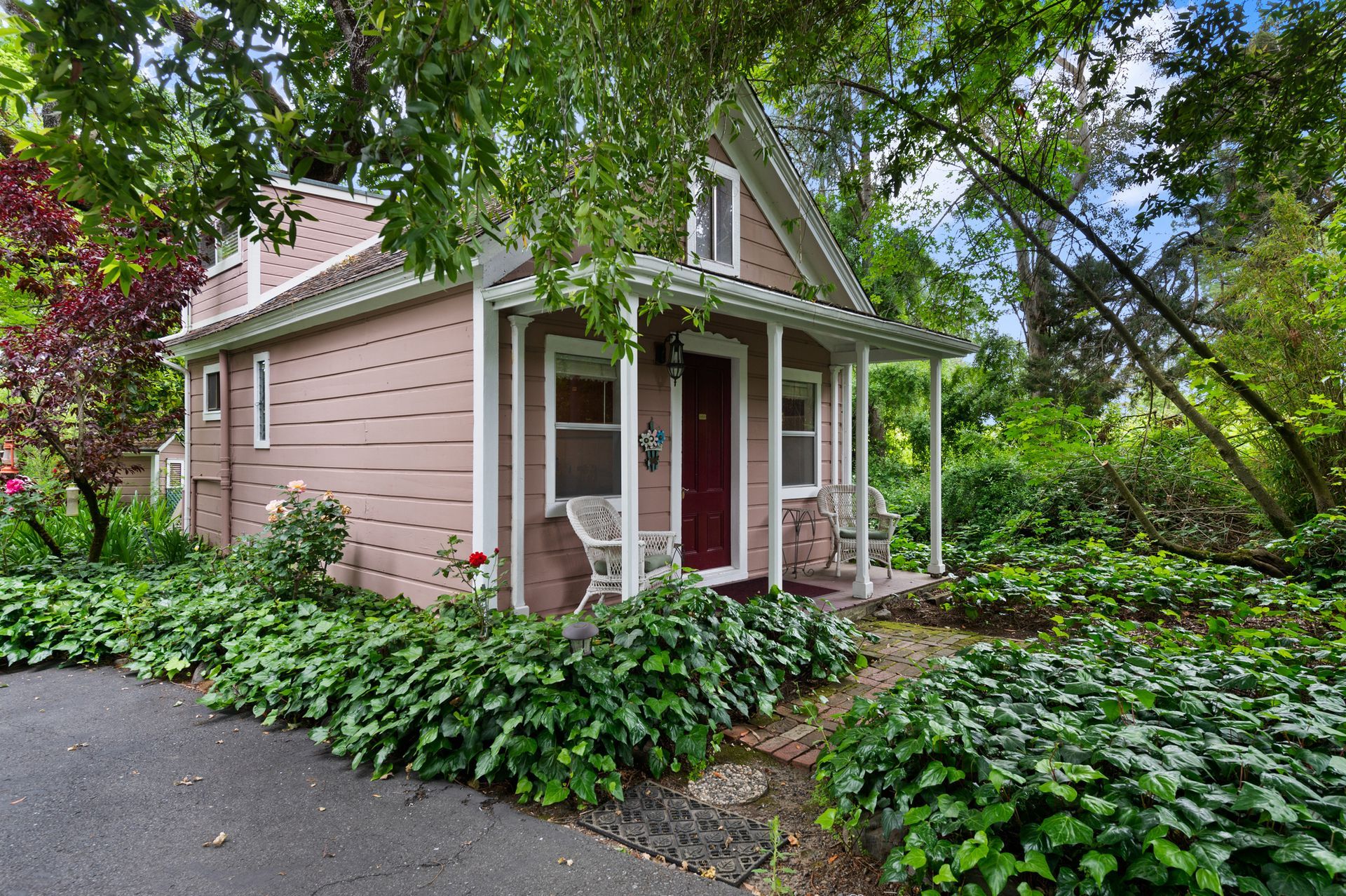 A small house with a porch is surrounded by trees and bushes.