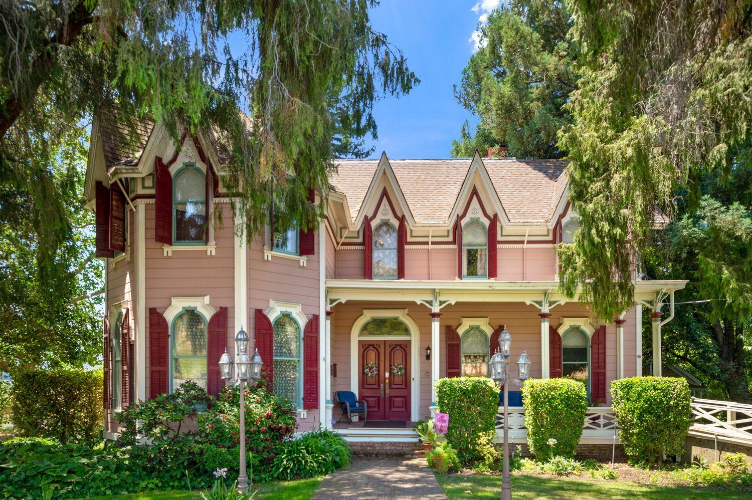 A large pink house with red shutters is surrounded by trees.