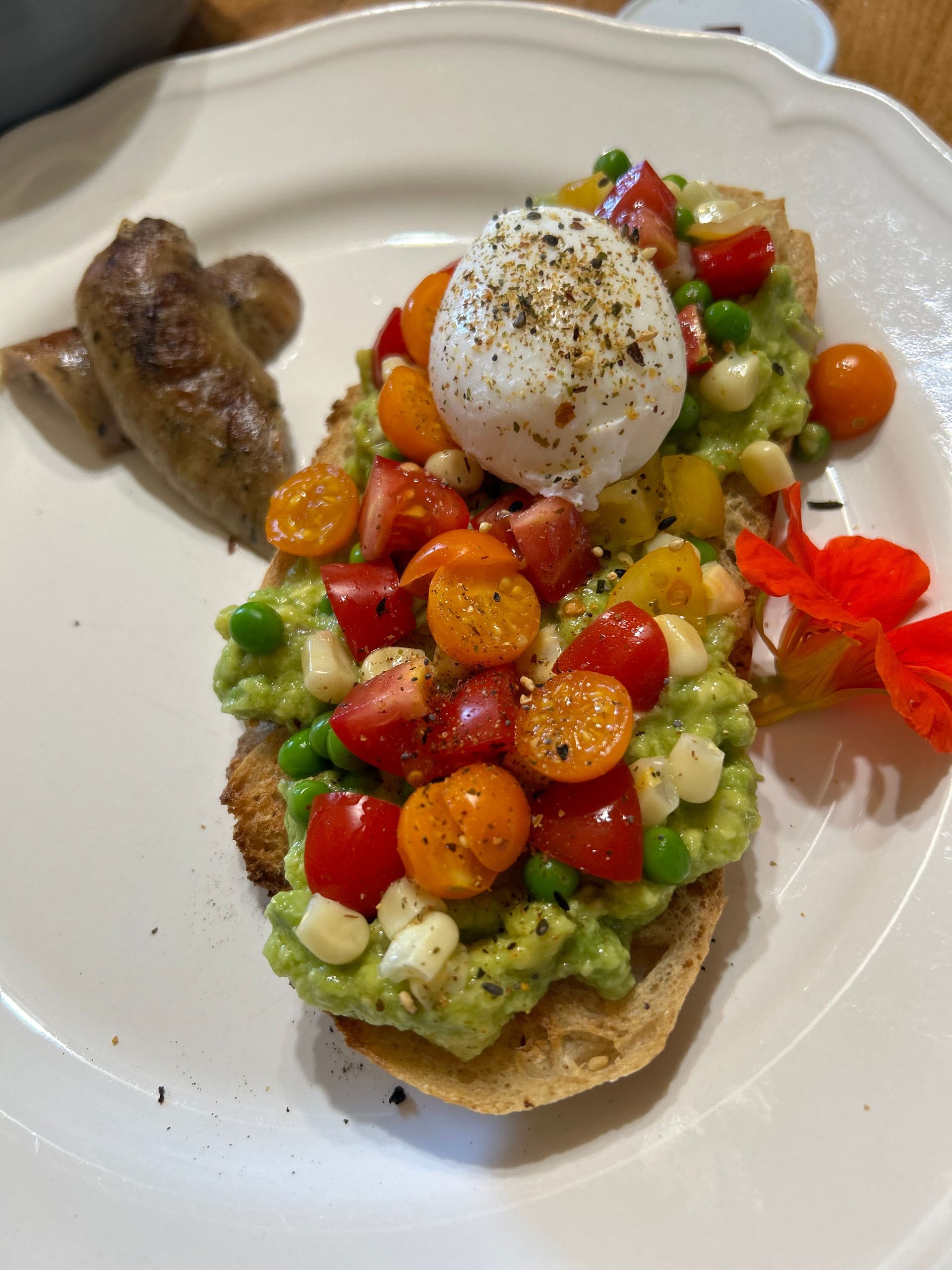 A white plate topped with avocado , tomatoes , and a poached egg.