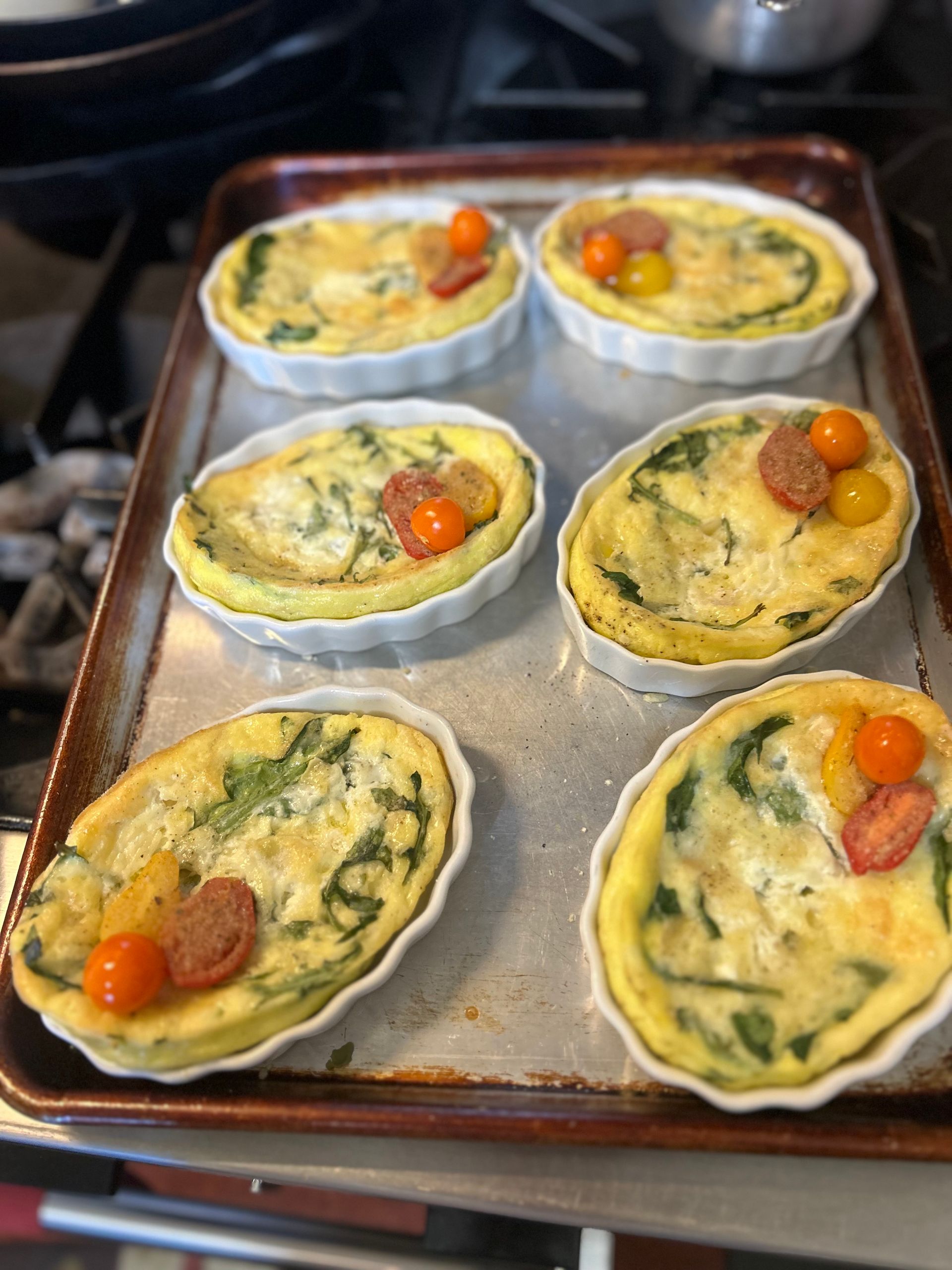 A bunch of quiches are sitting on a pan on a stove.