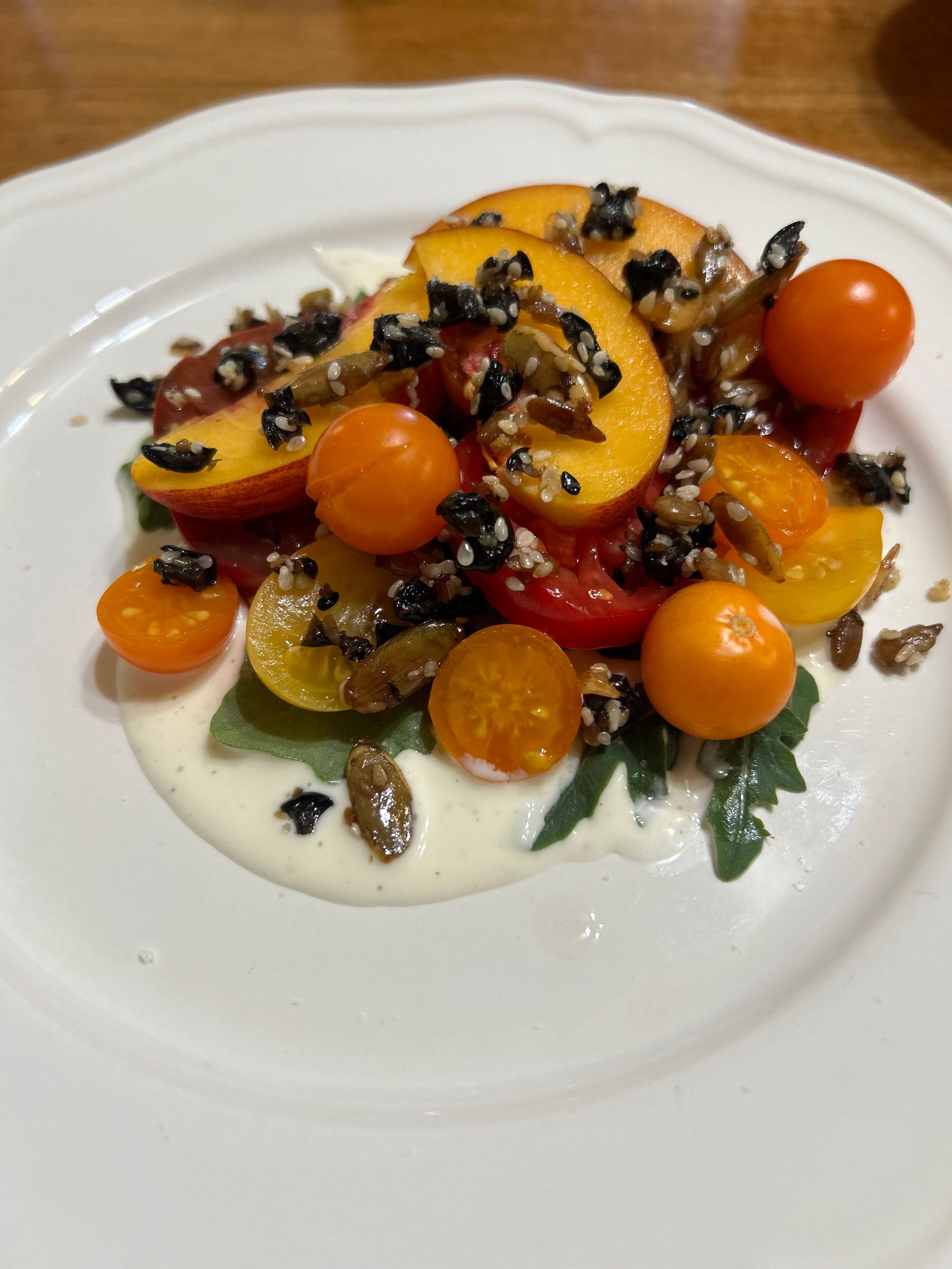 A white plate topped with a salad of peaches tomatoes and walnuts