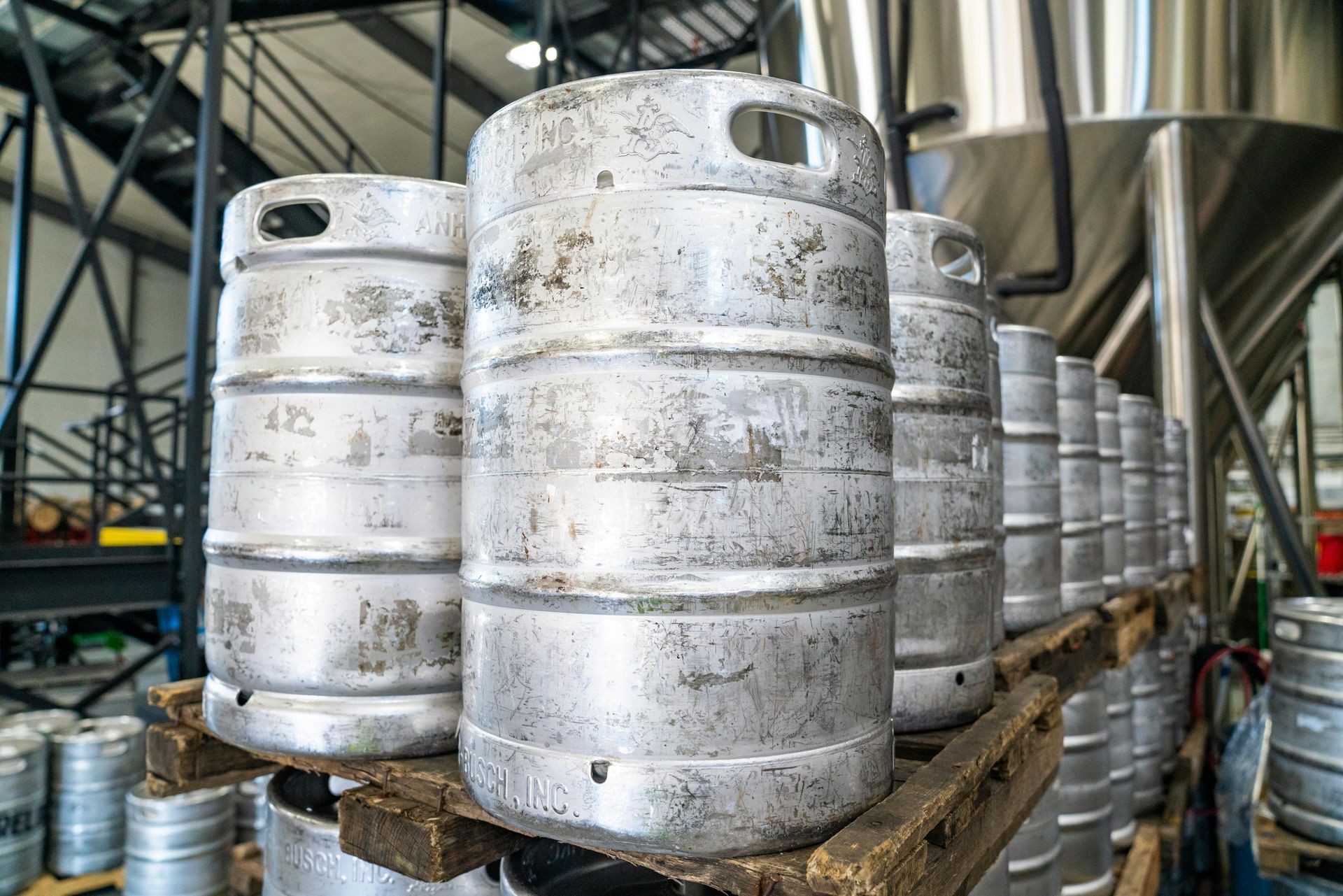 A bunch of kegs are stacked on top of each other on a wooden pallet in a brewery.