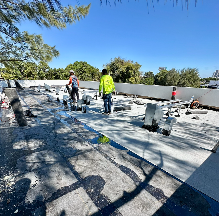 Workers on a flat roof repairing or installing roofing materials on a sunny day.