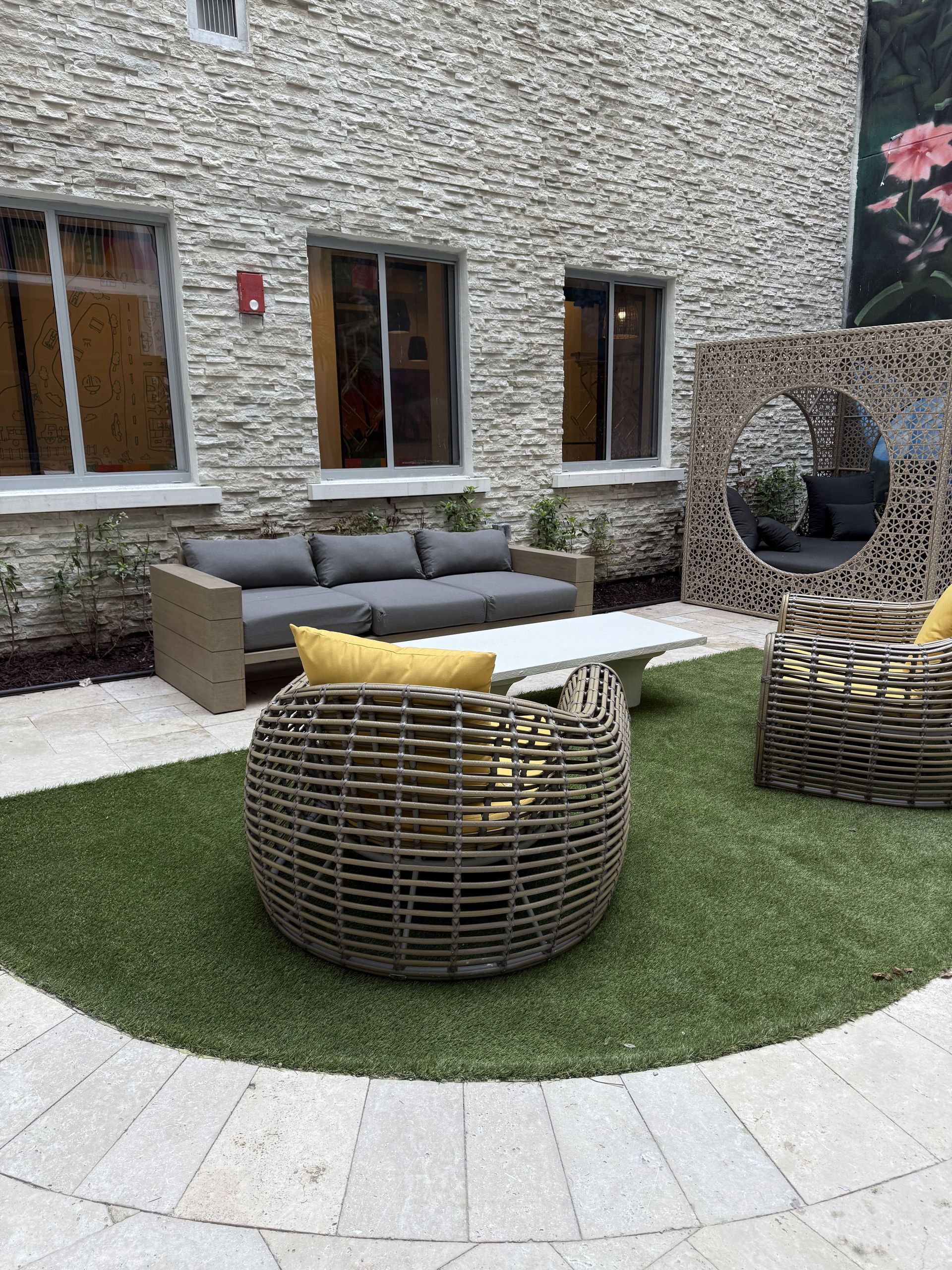 Outdoor seating area with gray sofa, wicker chairs, and artificial turf, against a stone wall.
