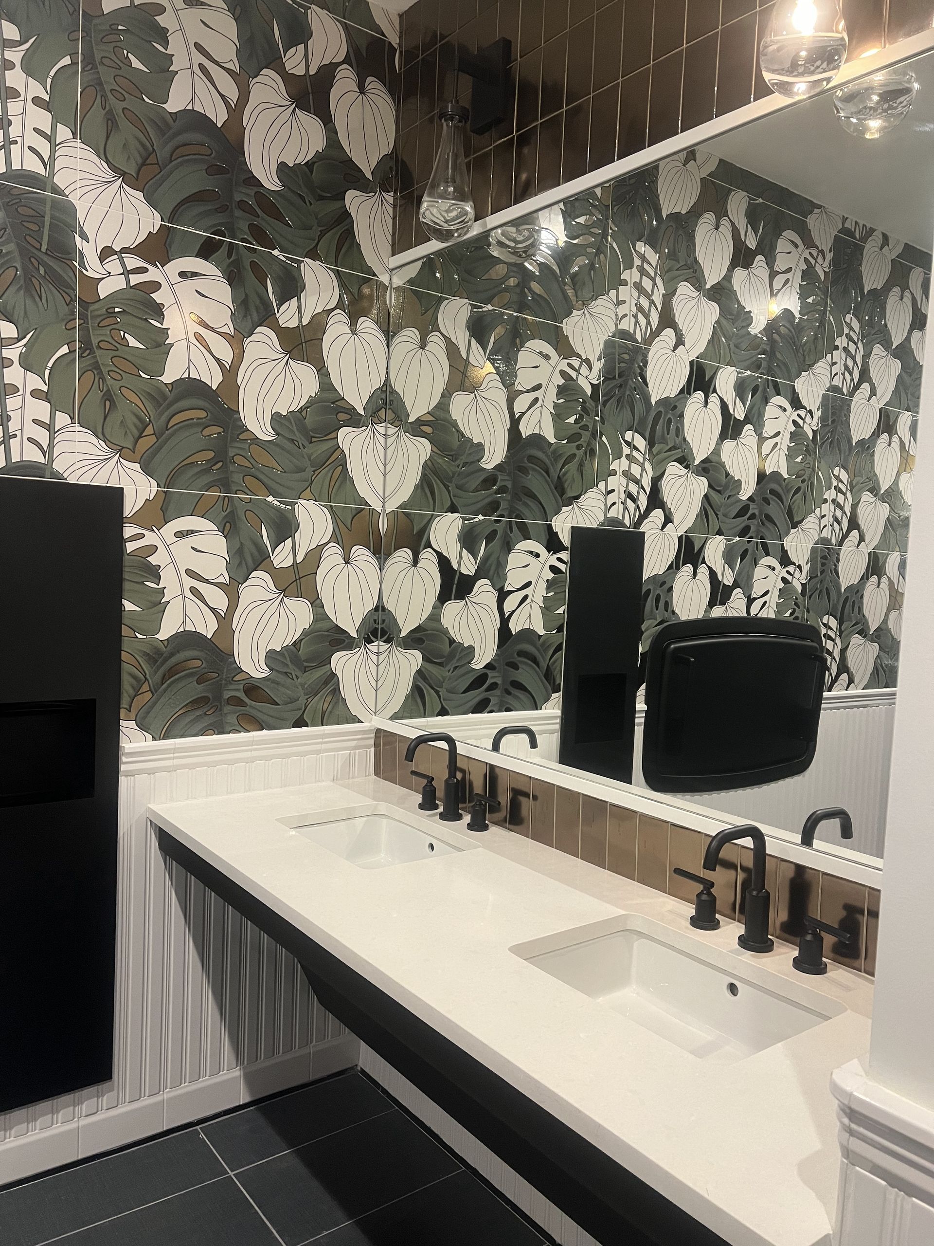 Bathroom with white countertop, black fixtures, leaf-patterned mirrored wall, and black accessories.