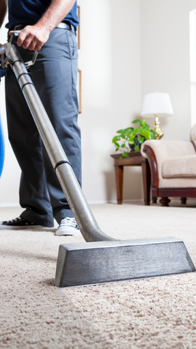 A man is using a vacuum cleaner to clean a carpet in a living room