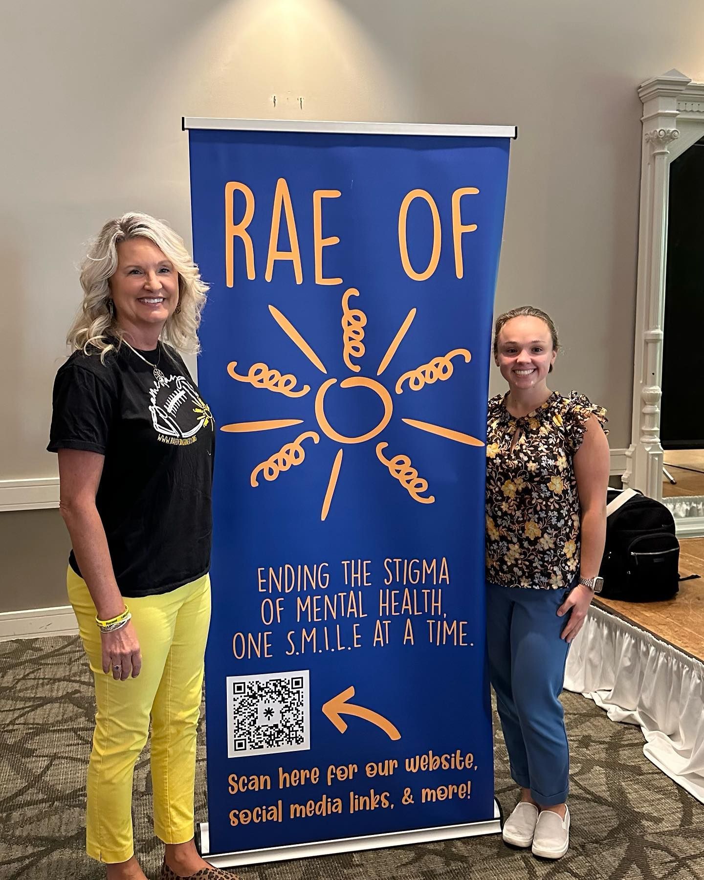 Two women stand by a blue banner for 