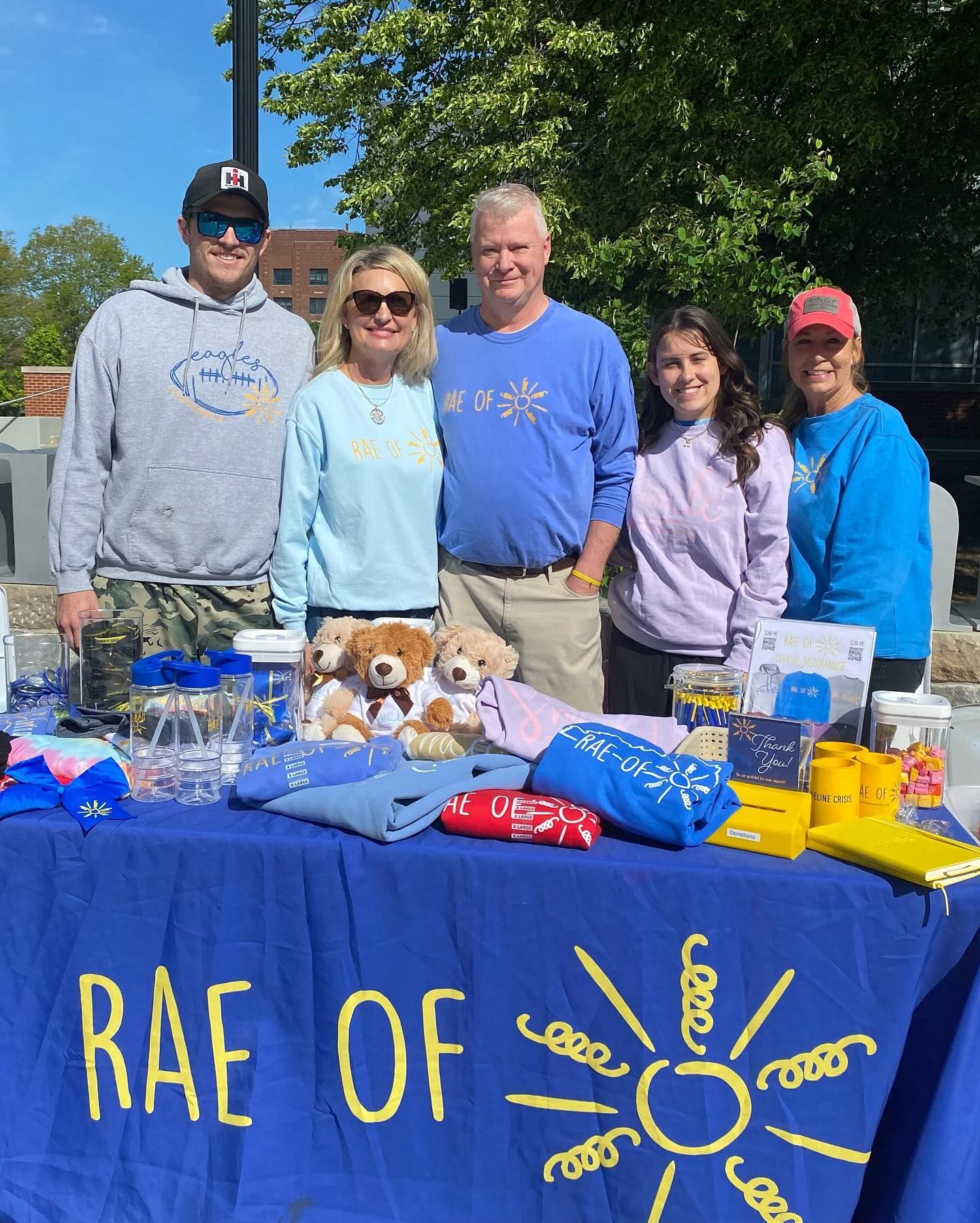 A group of five people smiling behind a table with merchandise, labeled 