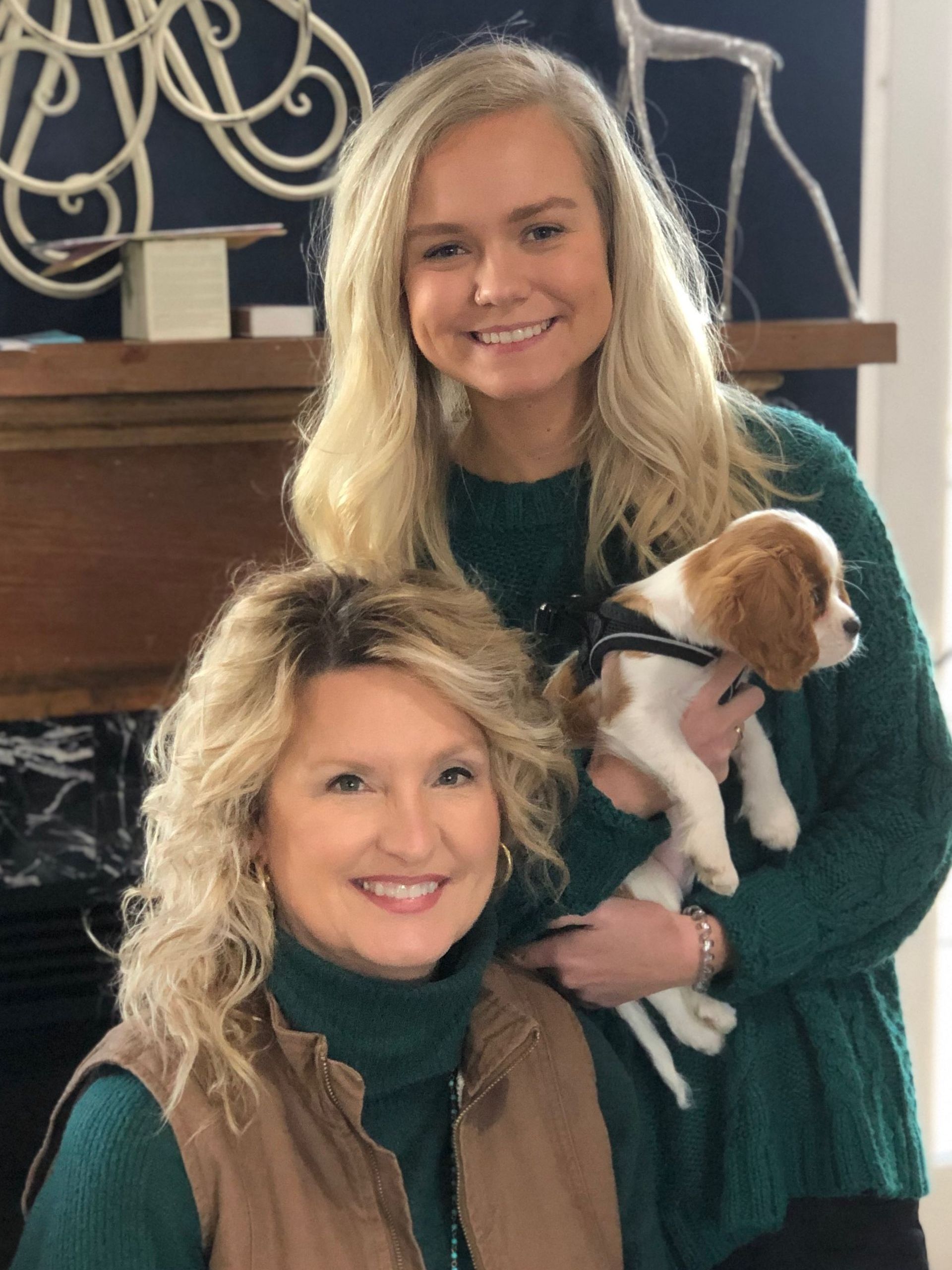 Two smiling blond women and a small Cavalier King Charles Spaniel puppy; one woman is holding the puppy.