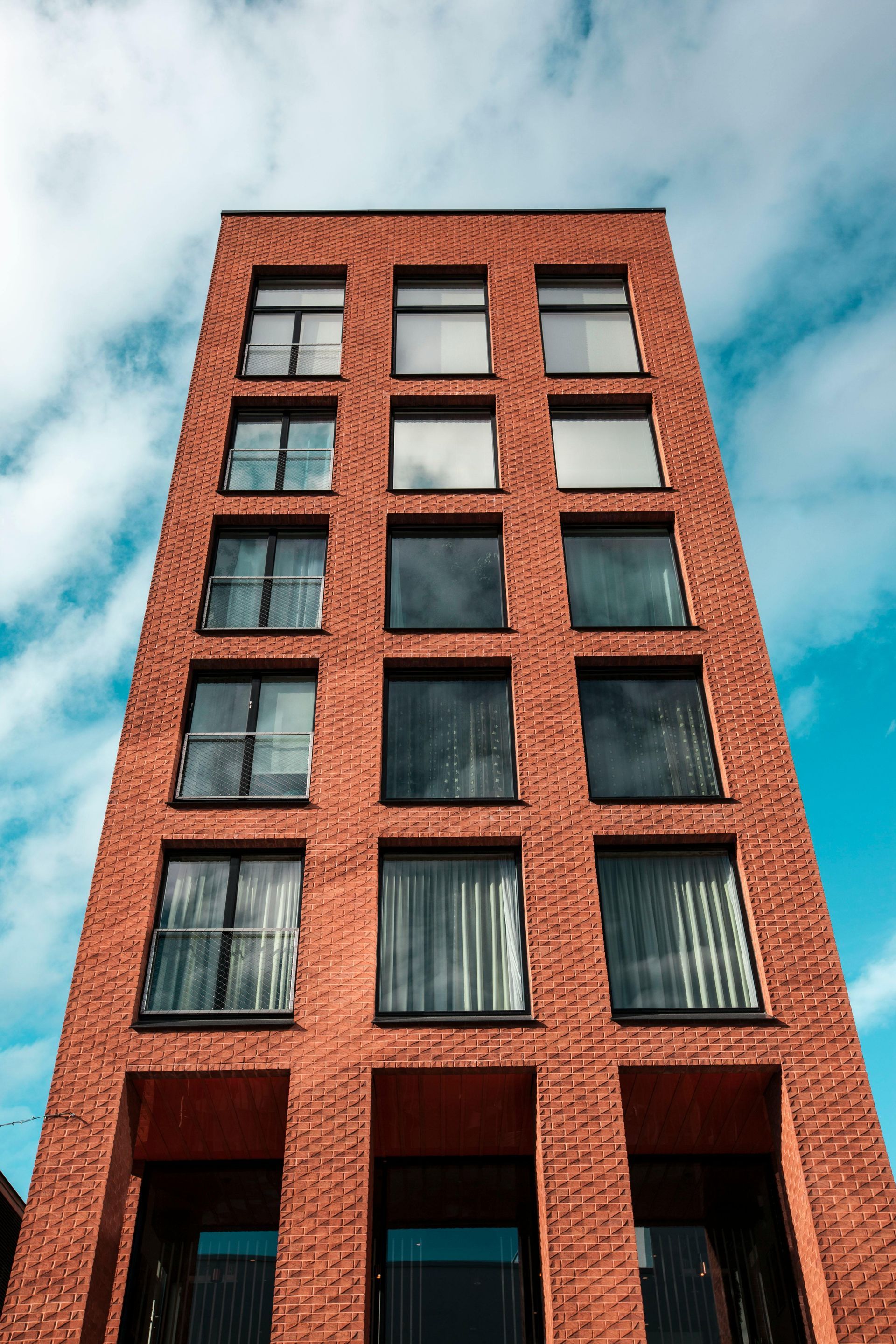 Tall brick building with multiple rectangular windows against a blue cloudy sky.