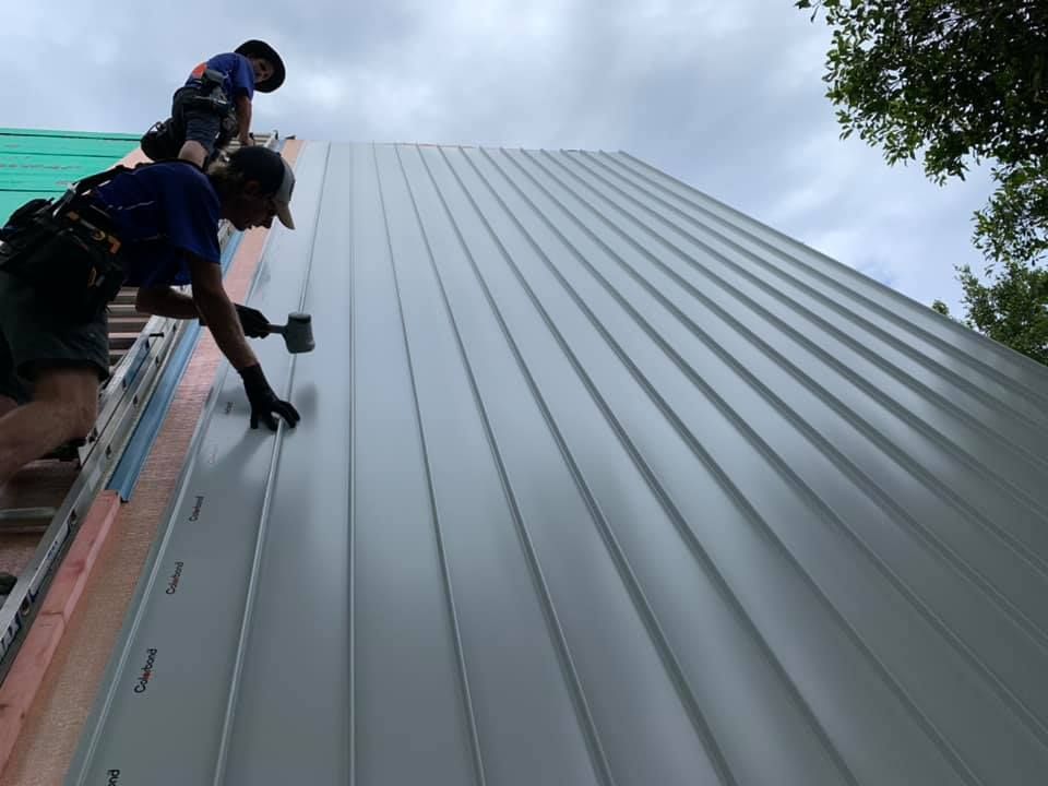 Two Workers Install Metal Roofing on a House Under a Cloudy Sky — Over the Top Roofing Specialists in Deception Bay, QLD