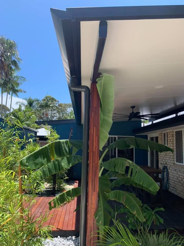 Patio With Banana Leaves, Black Gutter, Blue House, and Sunny Sky — Over the Top Roofing Specialists in North Lakes, QLD