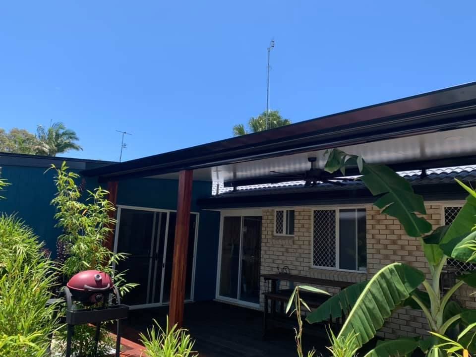 A Patio With a Grill, Plants, and a Black Roof Against a Blue Sky — Over the Top Roofing Specialists in Kallangur, QLD