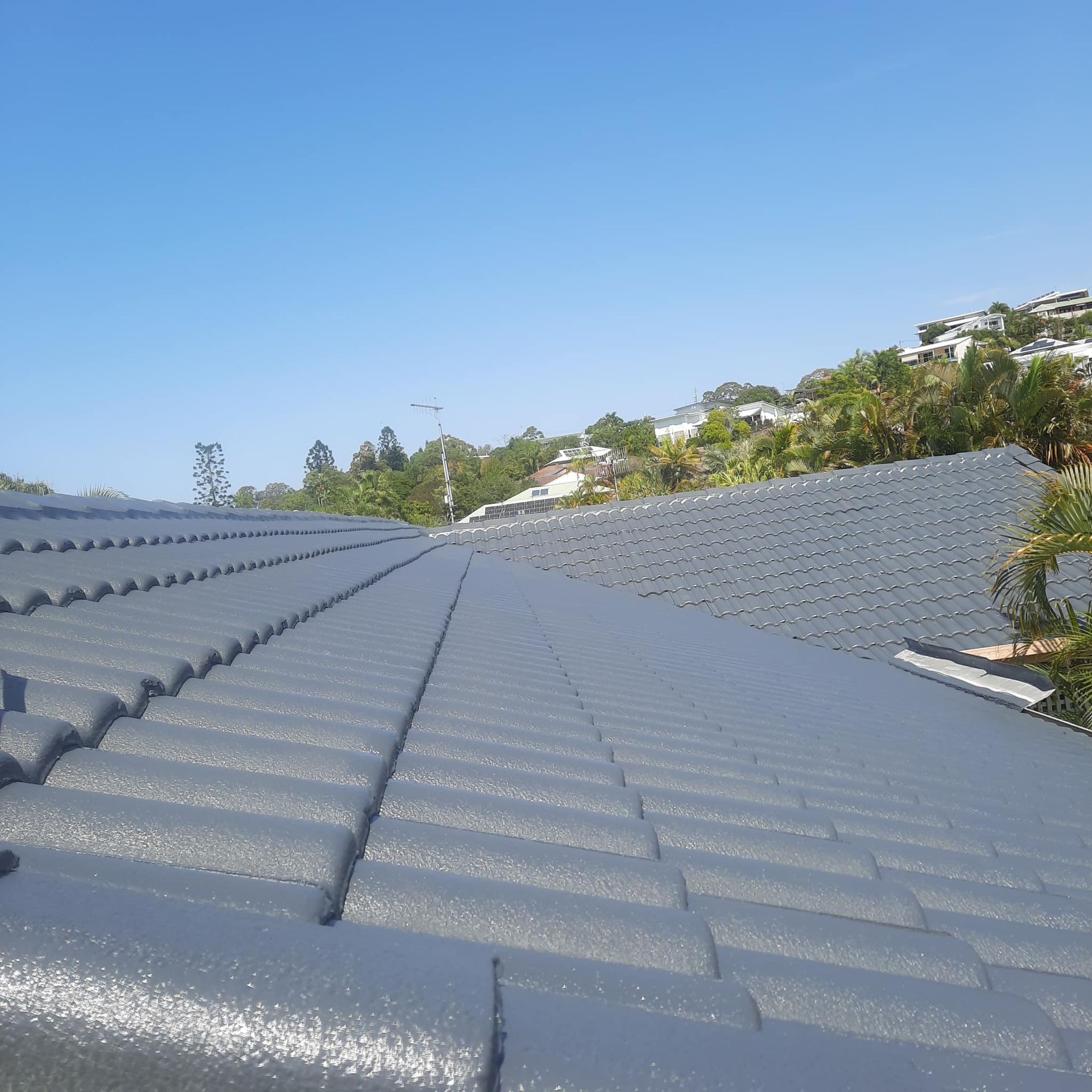 Gray Tiled Roof on a Sunny Day With a Backdrop of Hillside Homes — Over the Top Roofing Specialists in Nambour, QLD