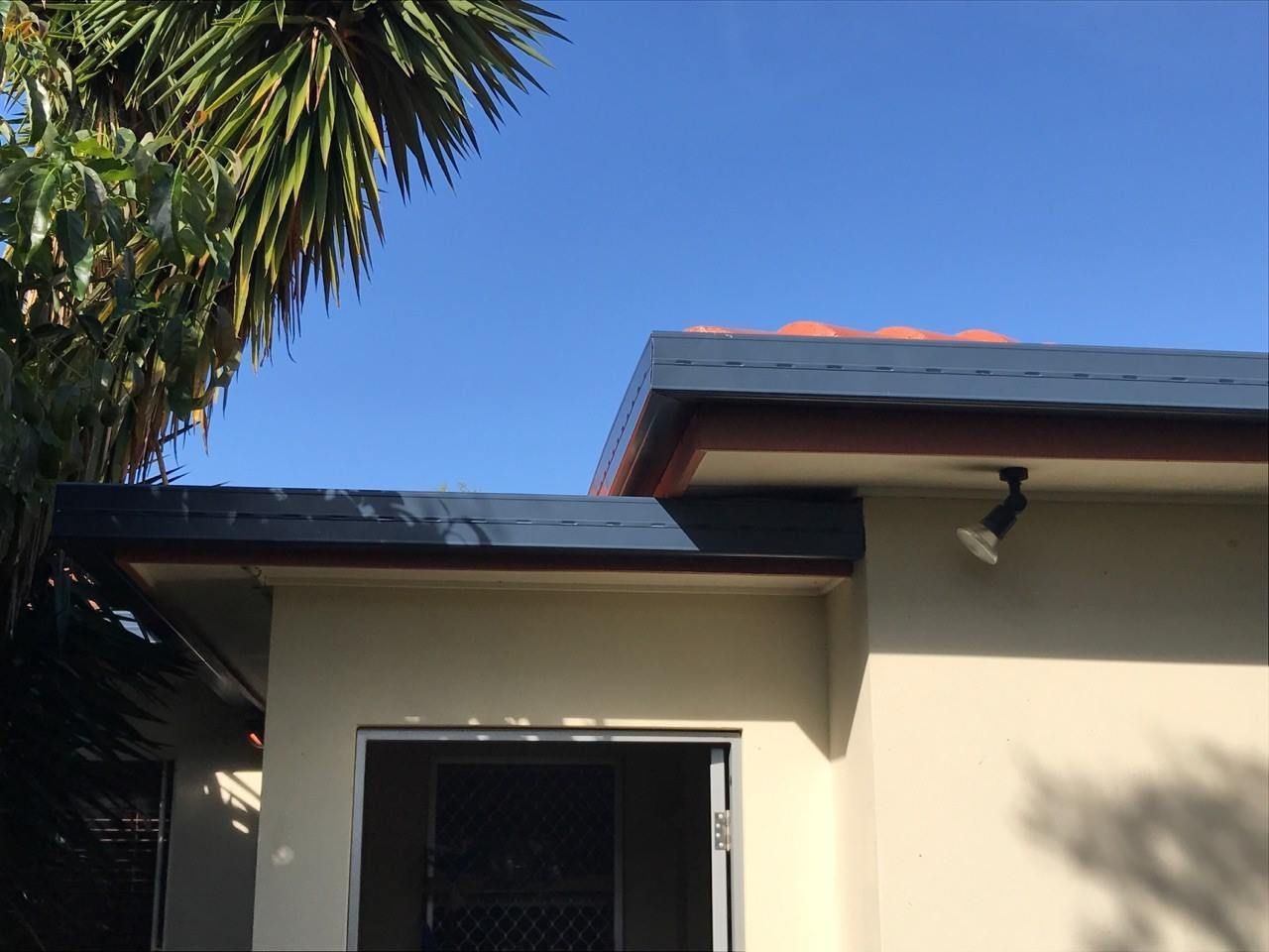 Beige Building With a Blue Roof and Brown Trim Against a Bright Blue Sky — Over the Top Roofing Specialists in Nambour, QLD