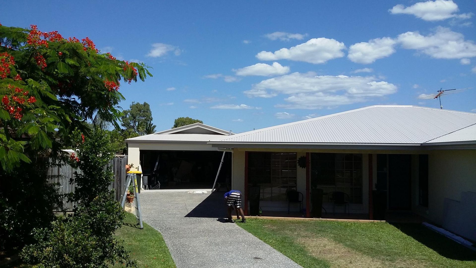 Man Cleaning Windows of a House With a Driveway, Blue Sky With Clouds — Over the Top Roofing Specialists in Maroochydore, QLD