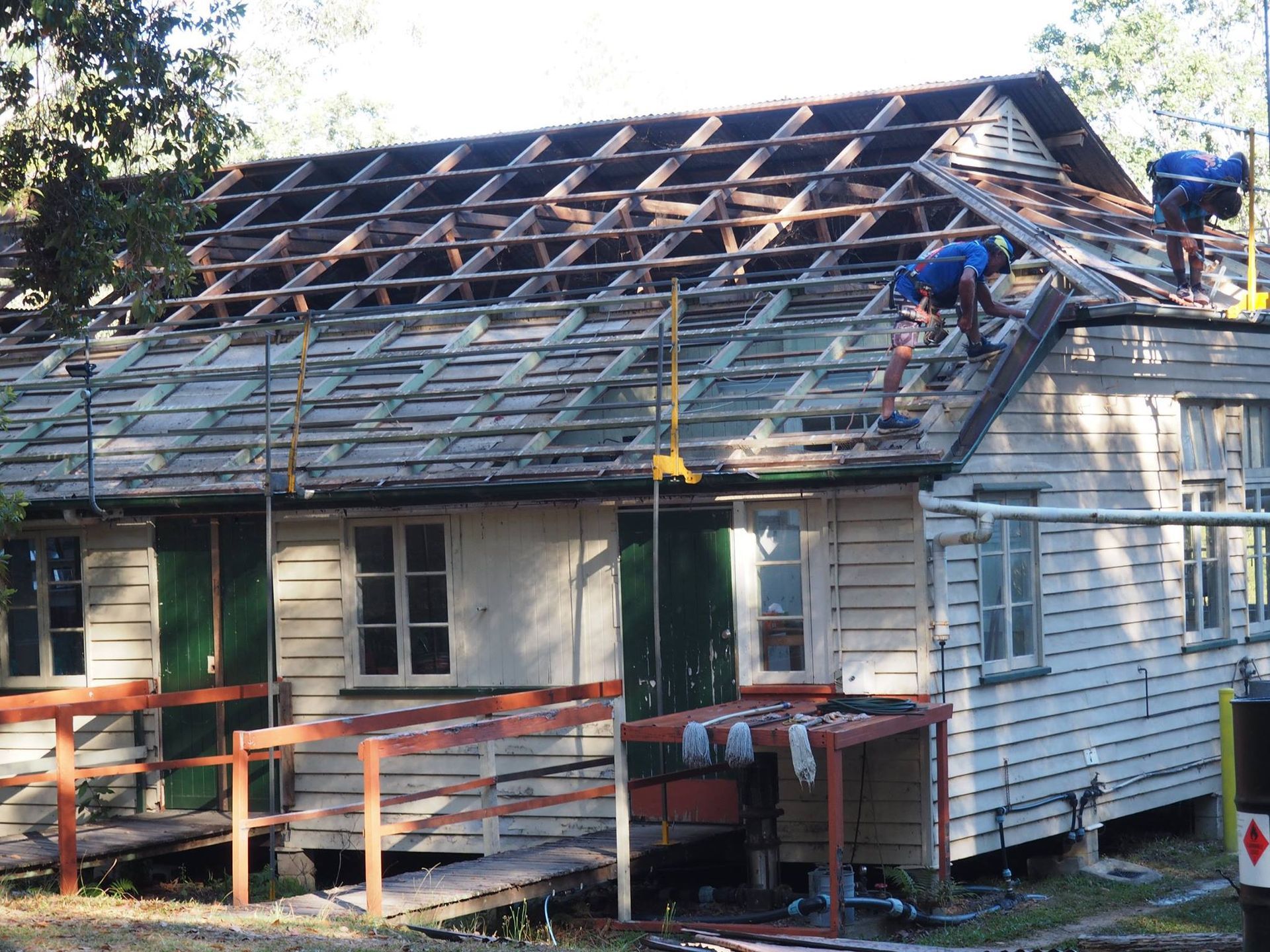 Men Removing a Roof From a Light-colored Wooden Building — Over the Top Roofing Specialists in Kunda Park, QLD