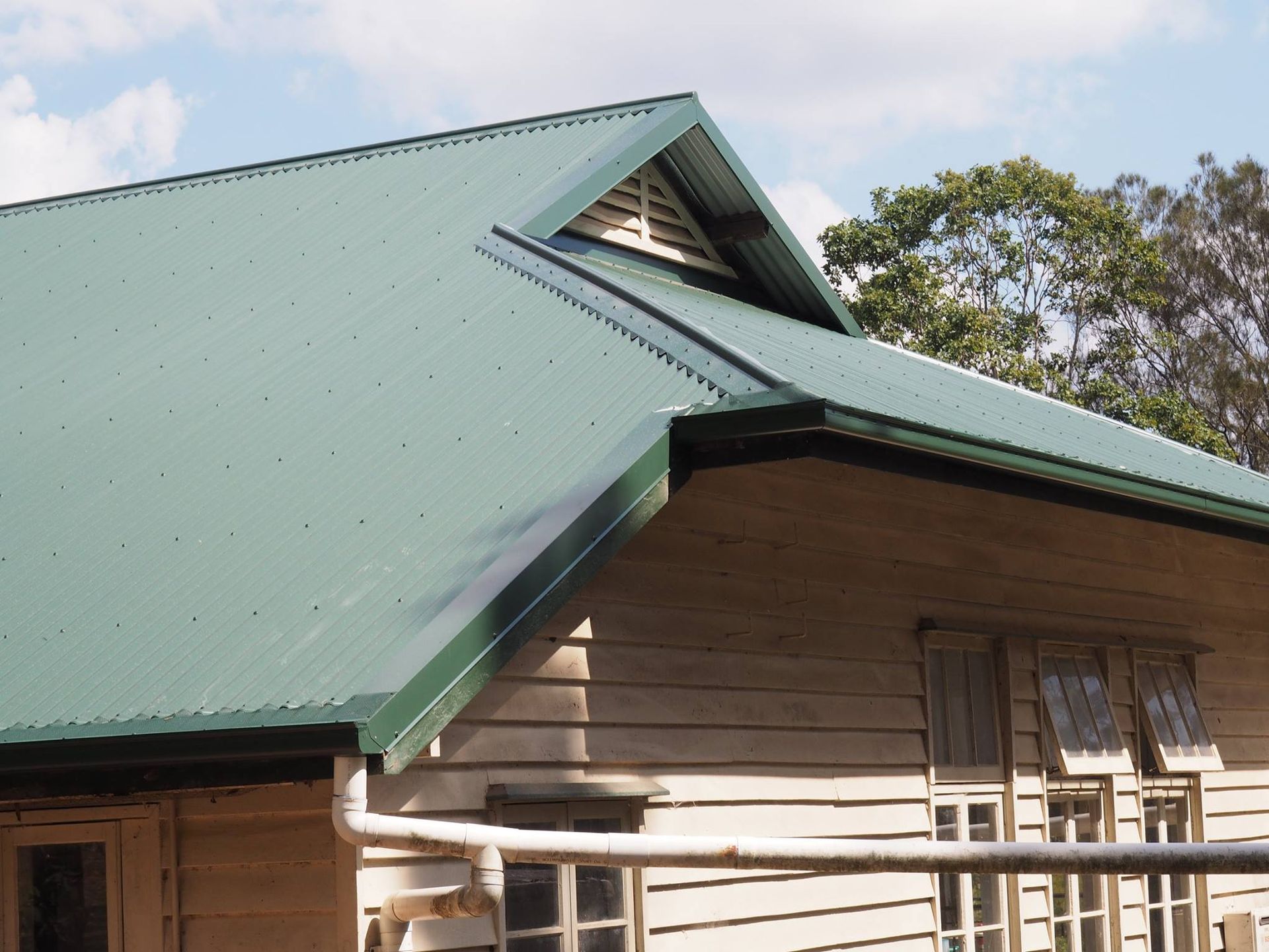 Green Metal Roof on a Light-colored Wooden Building — Over the Top Roofing Specialists in Narangba, QLD
