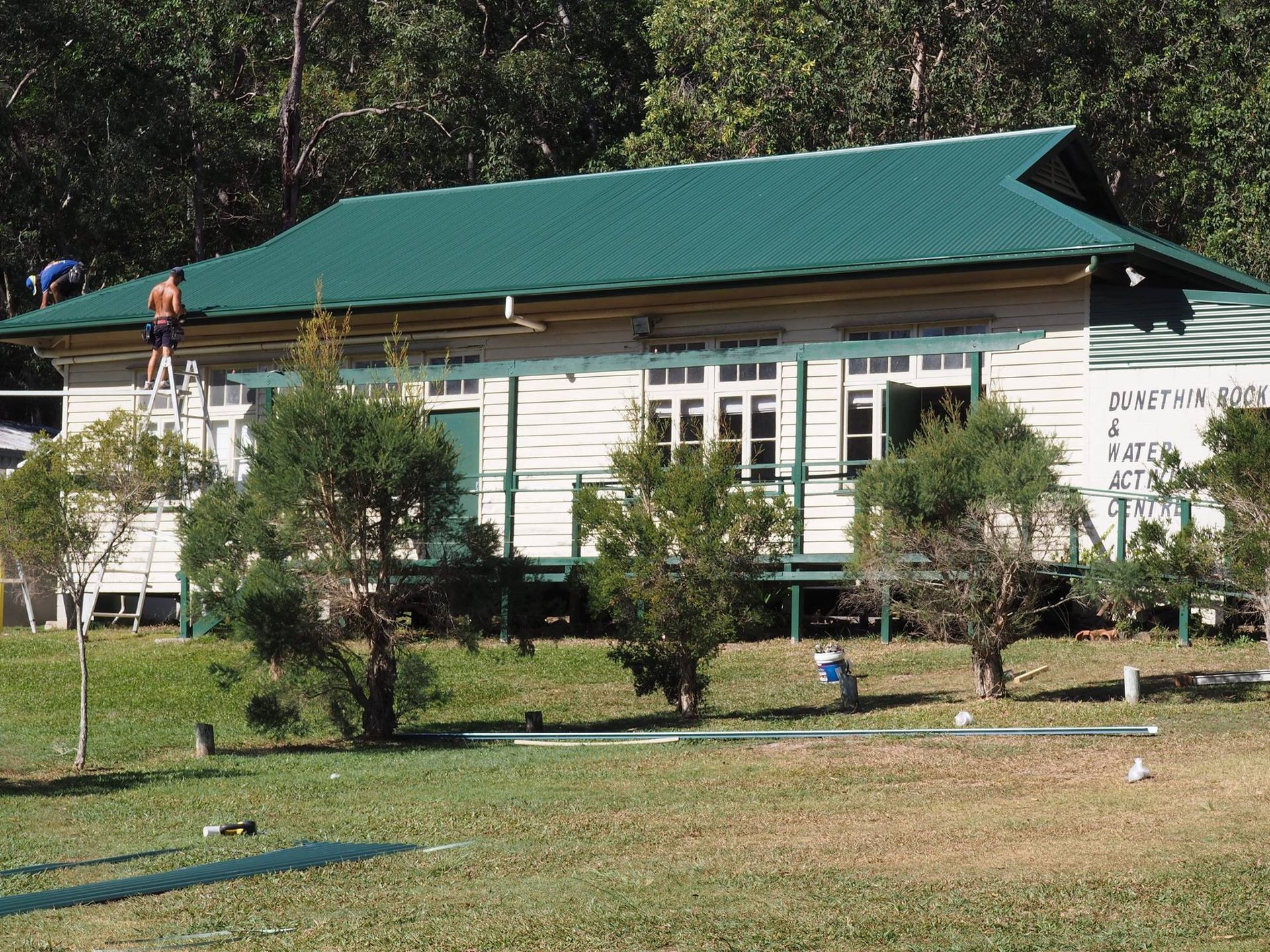 A Building With a Green Roof, Person on a Ladder Working on the Side — Over the Top Roofing Specialists in Deception Bay, QLD