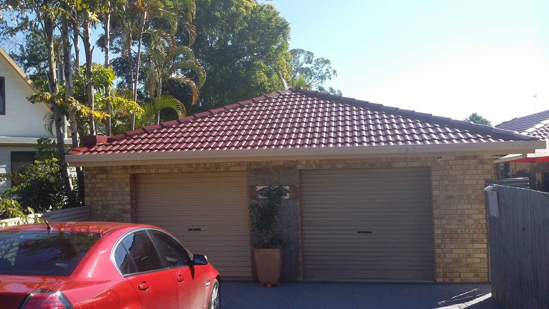 Red Car Parked in Front of a Two-car Garage With a Red Tiled Roof — Over the Top Roofing Specialists in Nambour, QLD