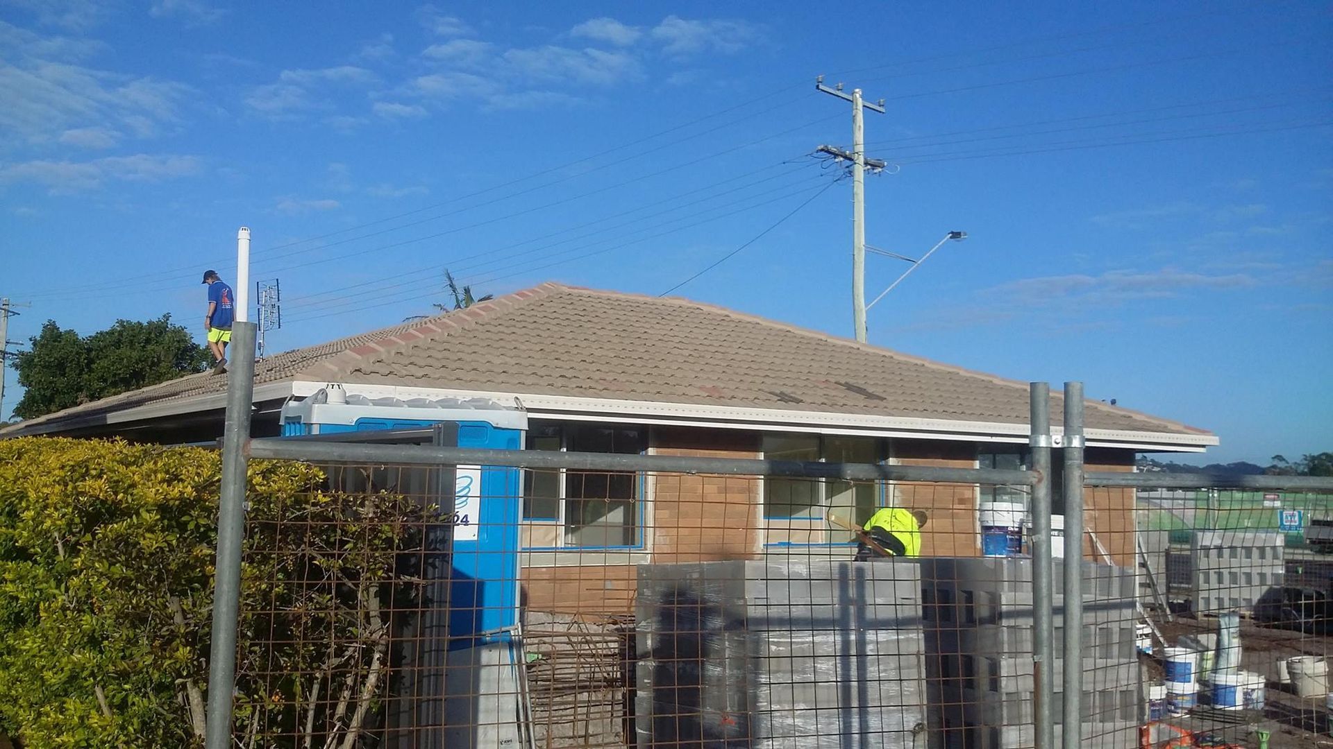 Building Under Construction With Workers on Roof and Stacked Materials — Over the Top Roofing Specialists in Nambour, QLD