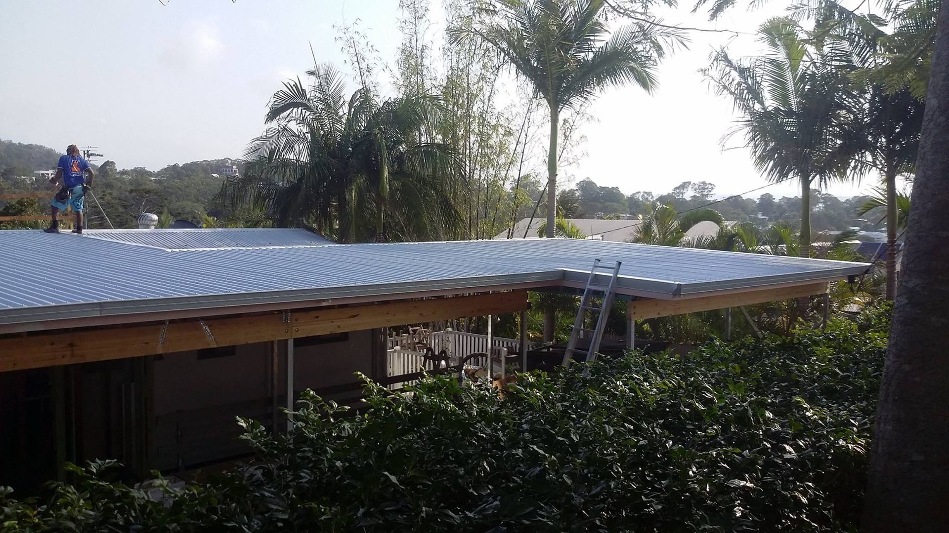 A Person Cleaning a Corrugated Metal Roof of a Building — Over the Top Roofing Specialists in Maroochydore, QLD