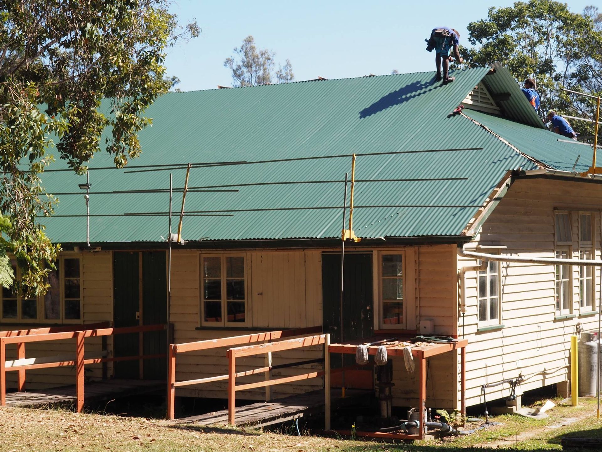 Workers Installing Green Corrugated Metal Roofing on a Wooden House — Over the Top Roofing Specialists in Buderim, QLD