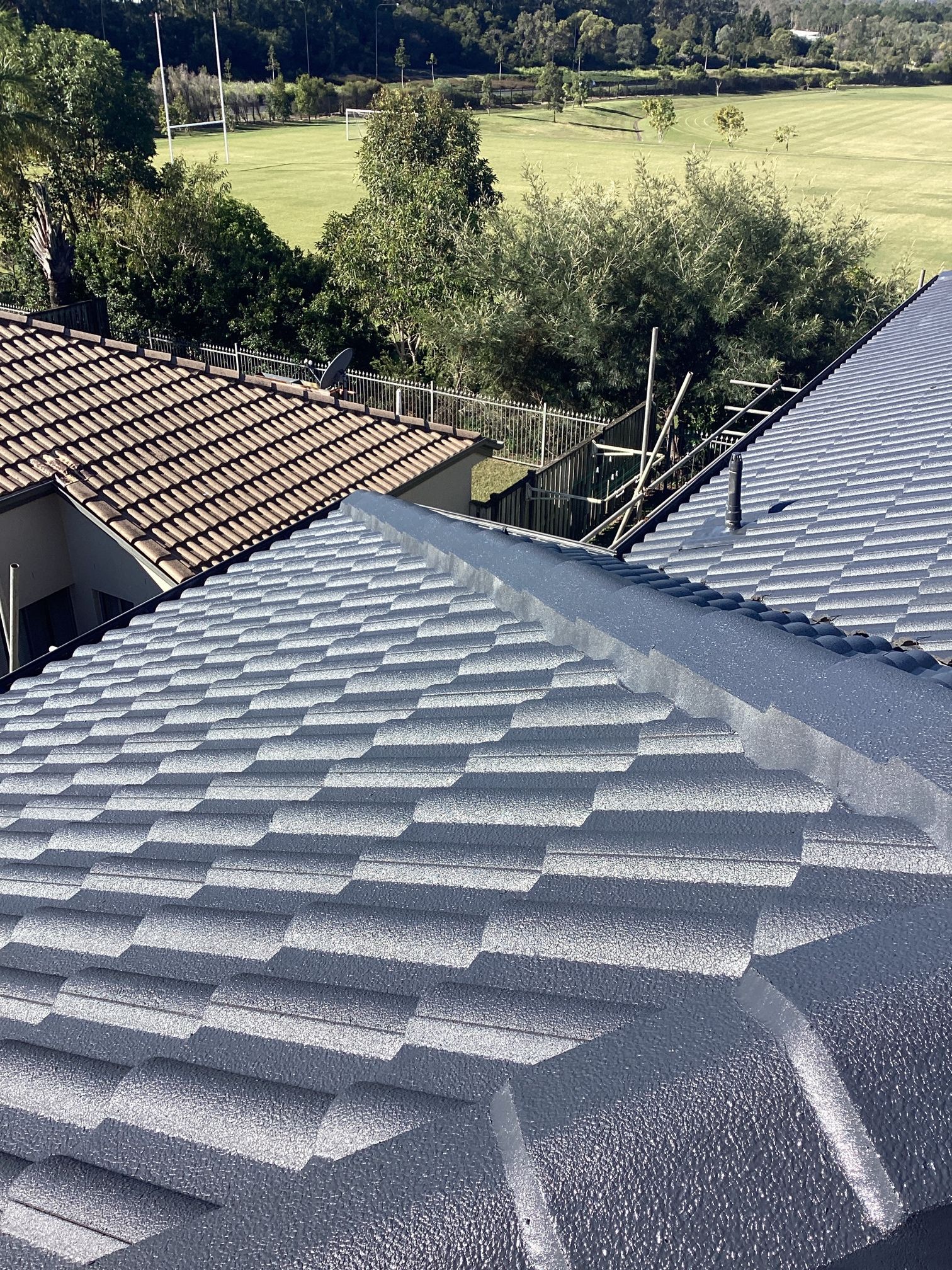 Gray roof tiles with a view of a green field and trees.