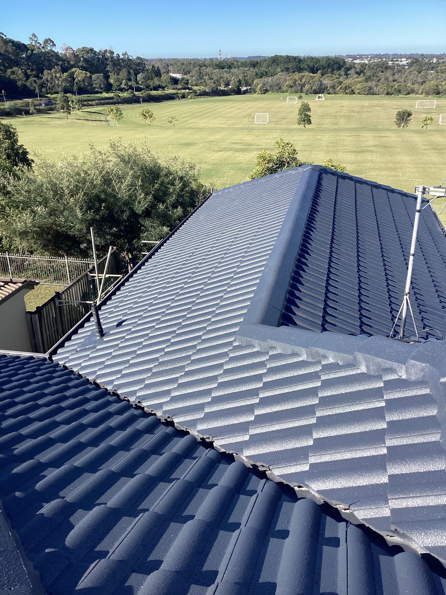 View of a dark gray tiled roof against a green landscape under a blue sky.