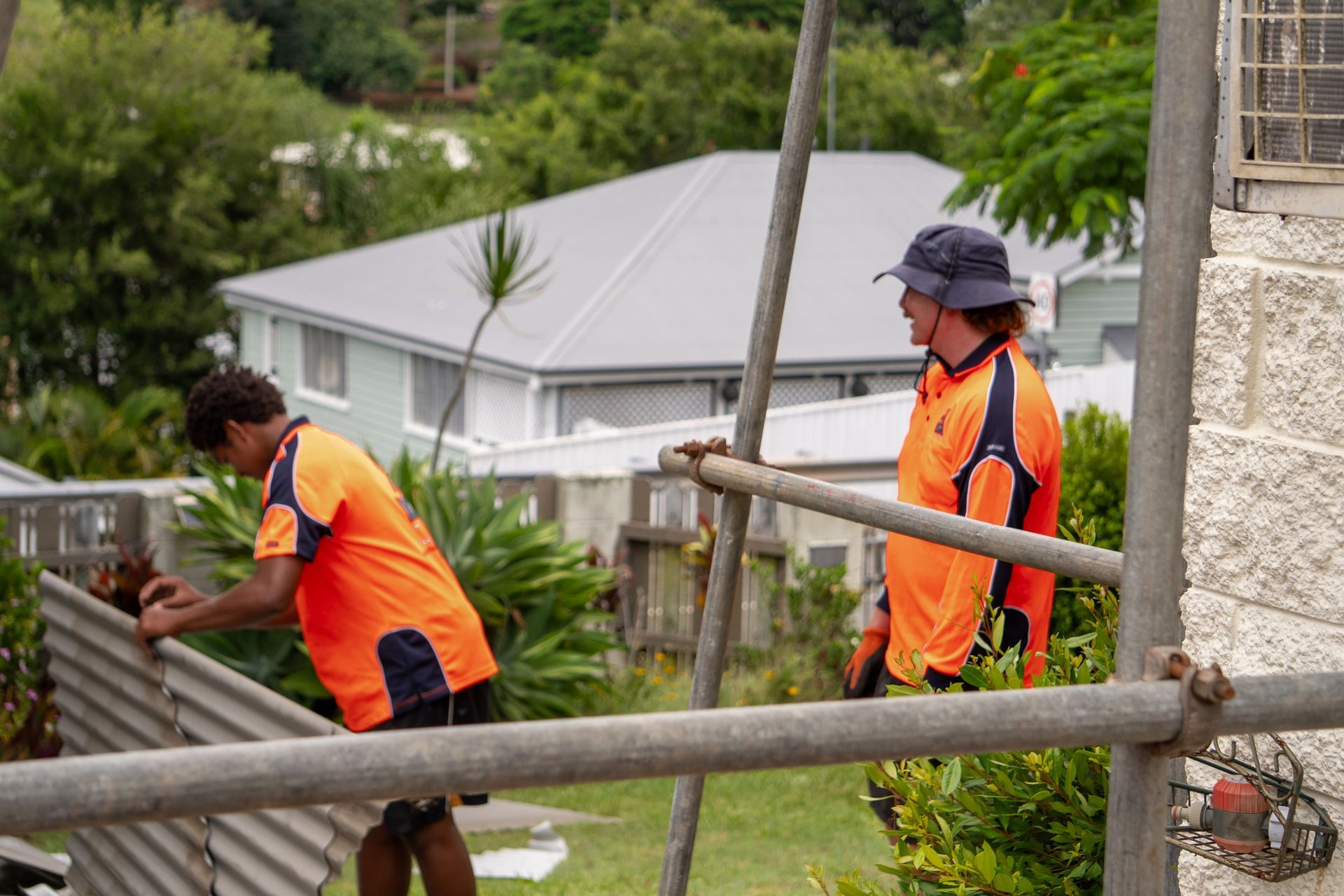 Two Workers Wearing Orange Shirts on Scaffolding — Over the Top Roofing Specialists in Kunda Park, QLD