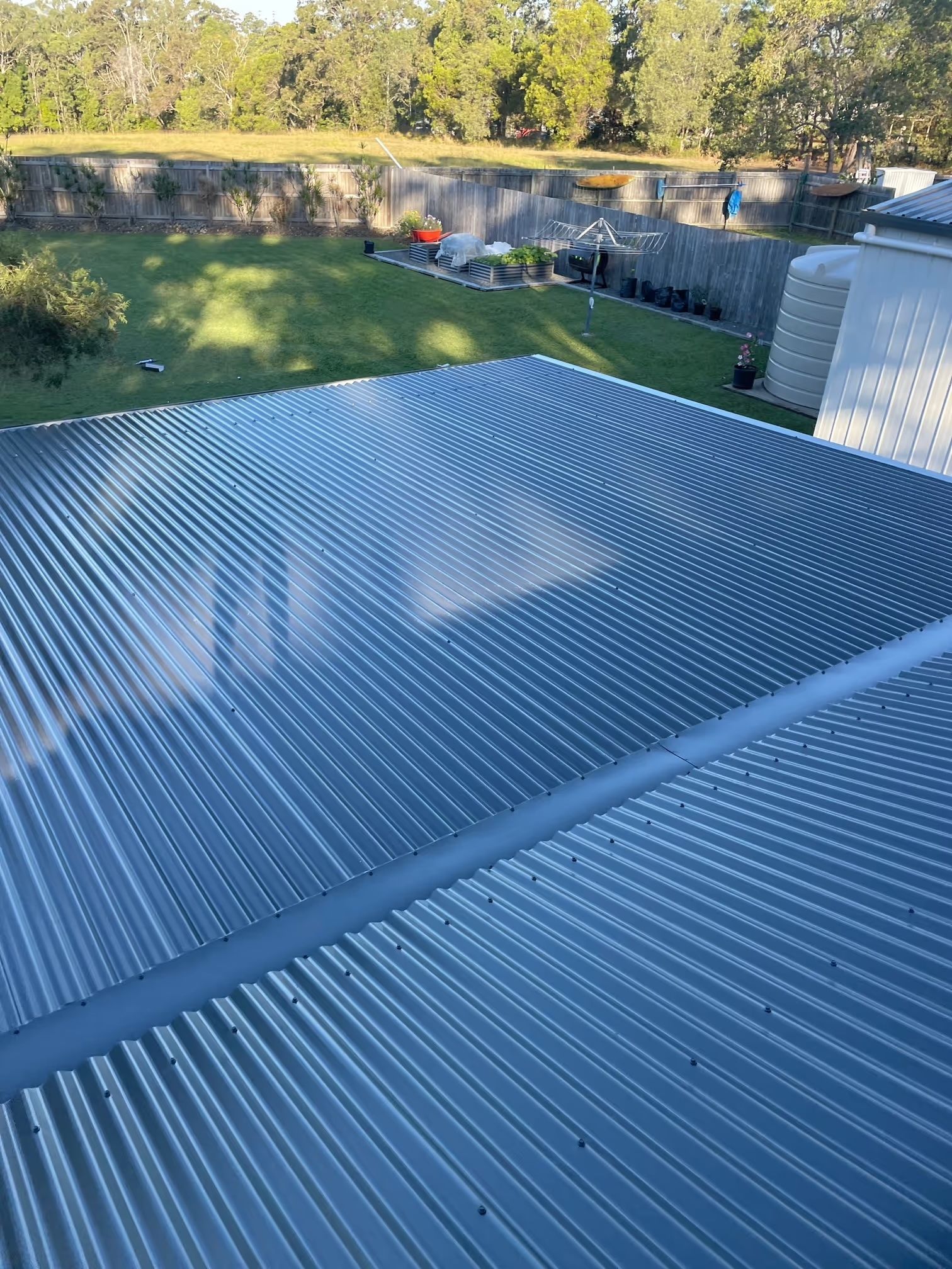 Corrugated metal roof with a backyard view featuring trees and a fence.