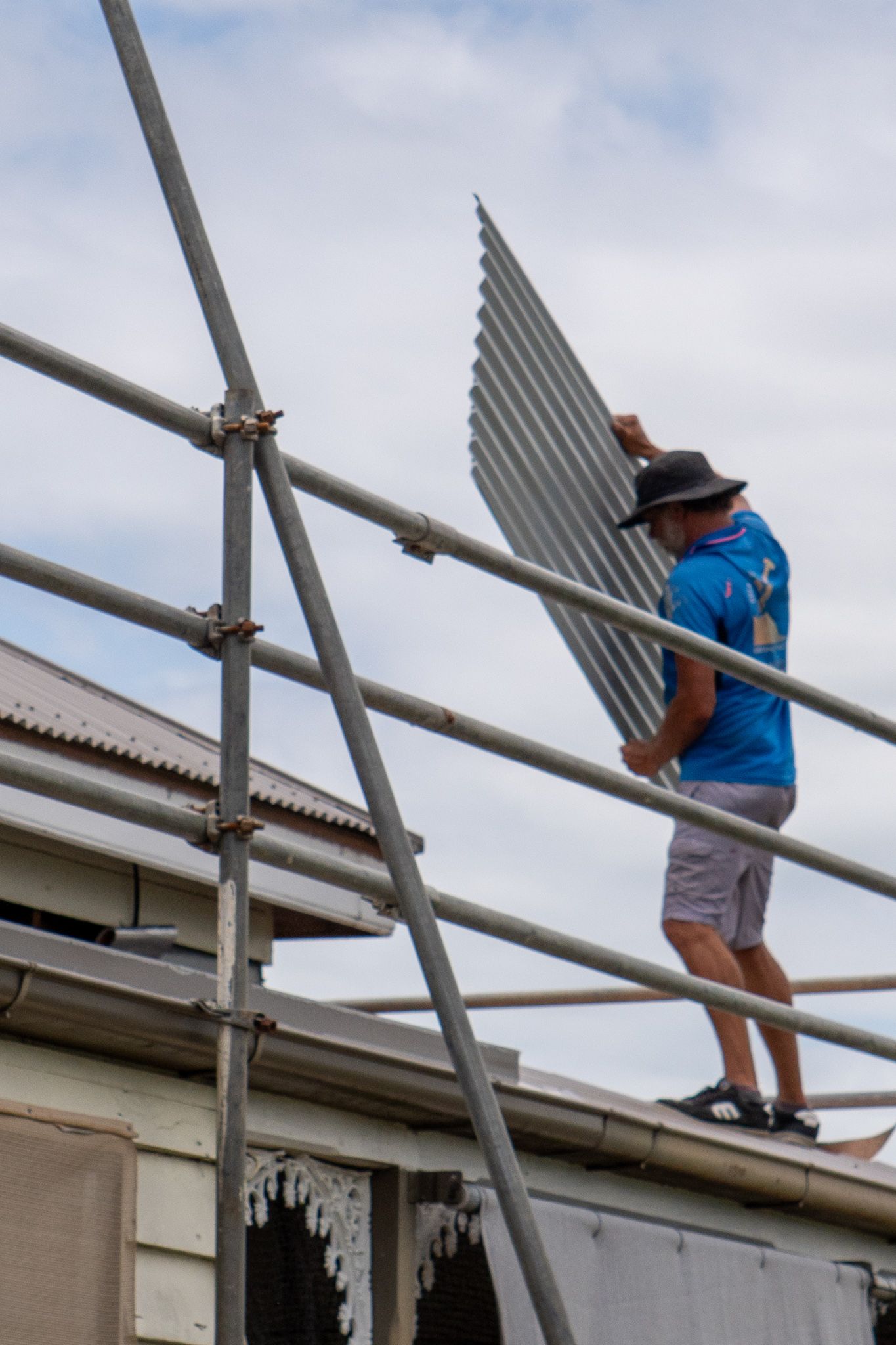 Person on Scaffolding Holds Corrugated Metal Sheet — Over the Top Roofing Specialists in Kunda Park, QLD