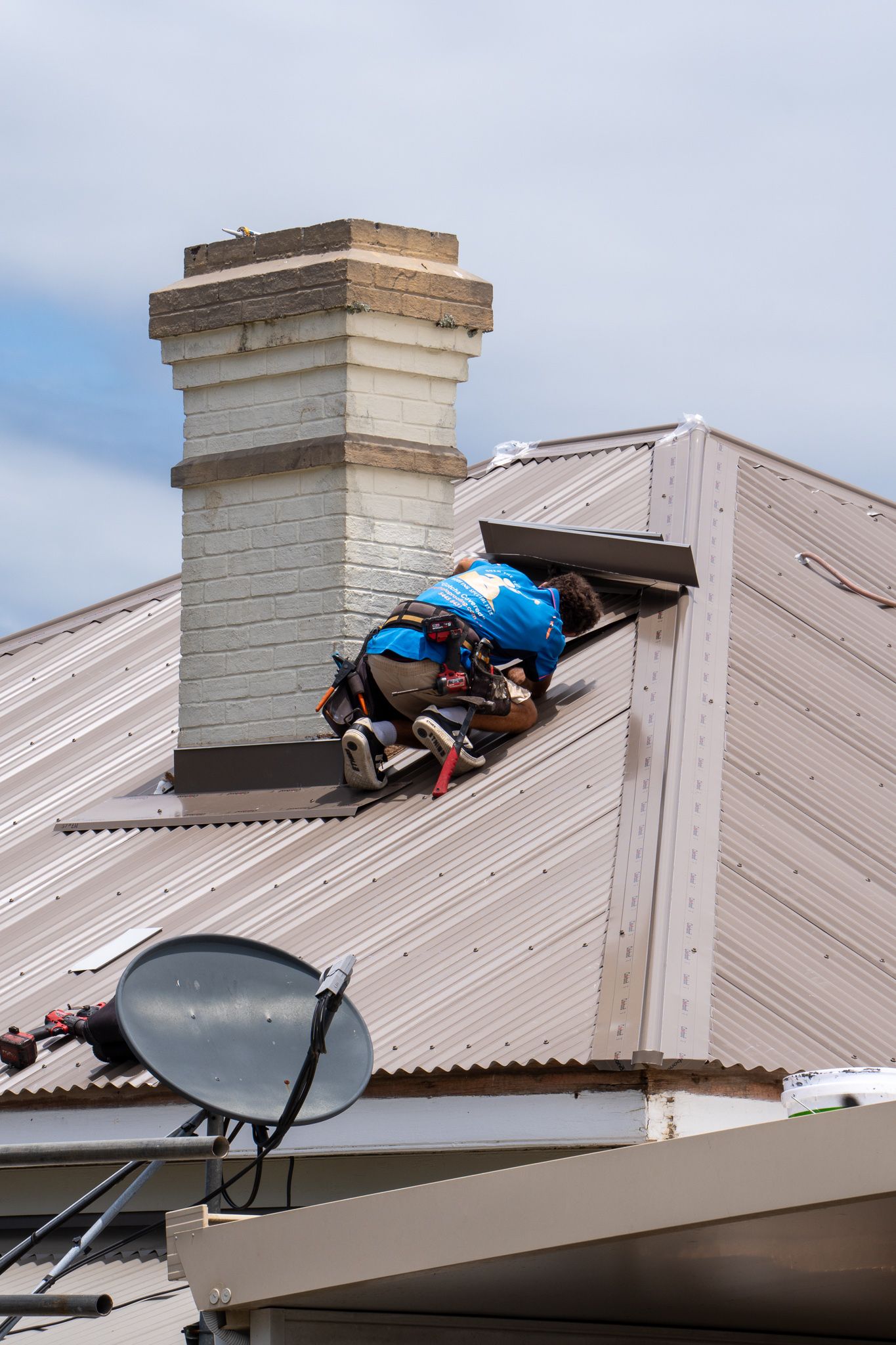 People working on roof near chimney and satellite dish; blue tarp and tools.