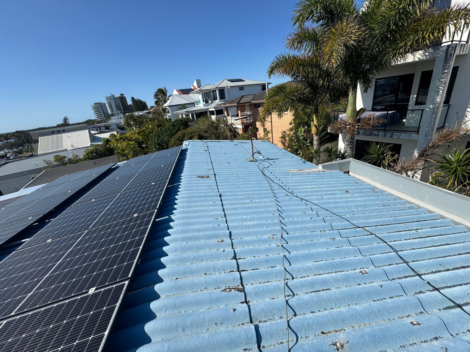 Blue Tiled Roof With Solar Panels, Houses, and Trees Under a Clear Sky — Over the Top Roofing Specialists in Kunda Park, QLD
