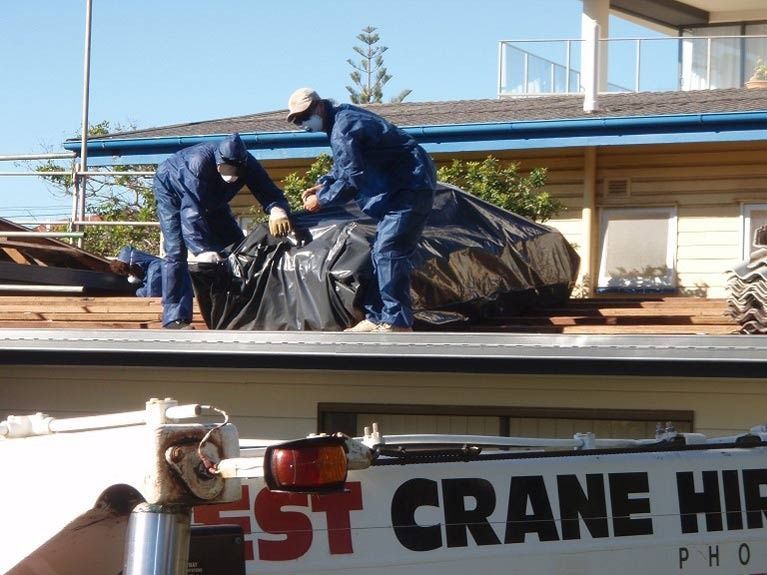 Workers in Suits on a Rooftop Placing Black Bags, Crane Truck Below — Over the Top Roofing Specialists in Deception Bay, QLD