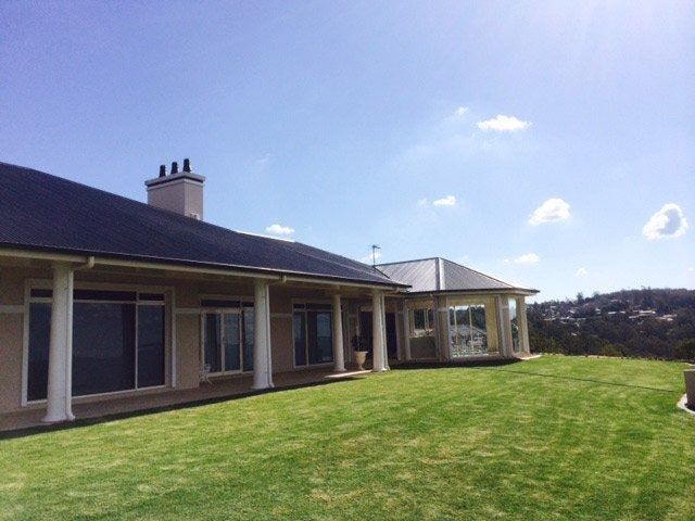 Large Beige House With Columns, Dark Roof, and Grassy Lawn on a Sunny Day — Over the Top Roofing Specialists in Buderim, QLD