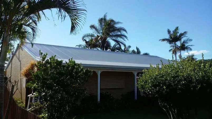 A Beige House With a Silver Roof, White Porch, and Palm Trees — Over the Top Roofing Specialists in Deception Bay, QLD
