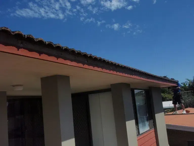 Roof of a Building With Dark Tiles and a Dark Gutter Against a Blue Sky — Over the Top Roofing Specialists in Morayfield, QLD