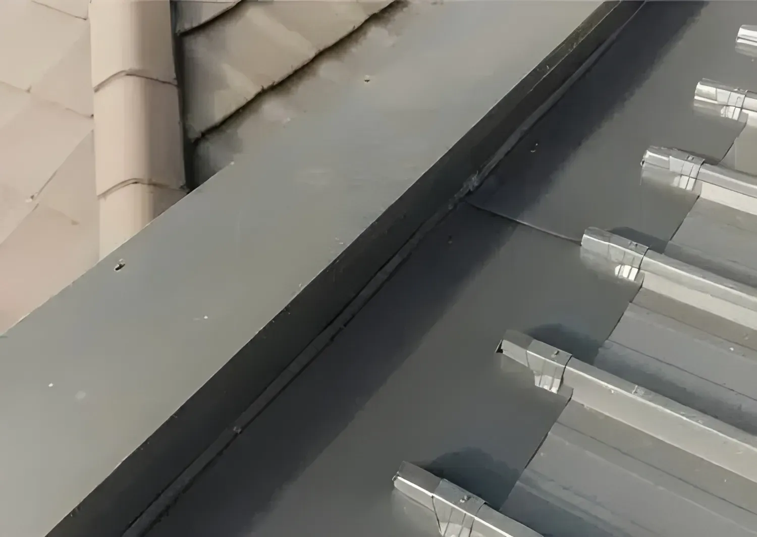 Gray Metal Roof With a Gutter and Adjacent Beige Tile Roof — Over the Top Roofing Specialists in Kunda Park, QLD