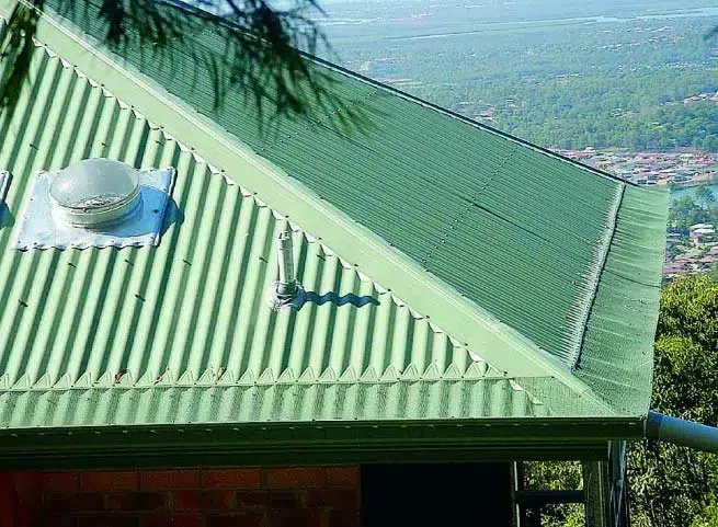 Green Corrugated Metal Roof With a Vent, Against a Blurred Hilltop View — Over the Top Roofing Specialists in Gympie, QLD