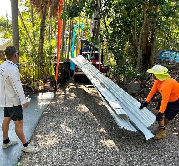 Two Workers Unloading Metal Sheets From a Truck on a Driveway — Over the Top Roofing Specialists in Caloundra, QLD