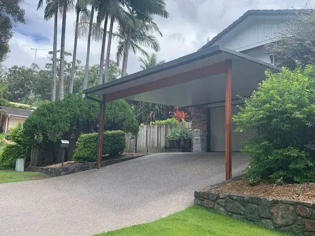Carport Over a Concrete Driveway Leading to a House With Trees and Bushes — Over the Top Roofing Specialists in Gympie, QLD