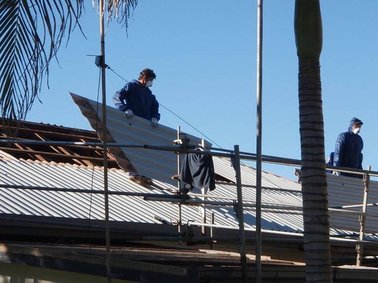 Two Workers in Blue Coveralls and Masks Replacing a Corrugated Metal Roof — Over the Top Roofing Specialists in Buderim, QLD