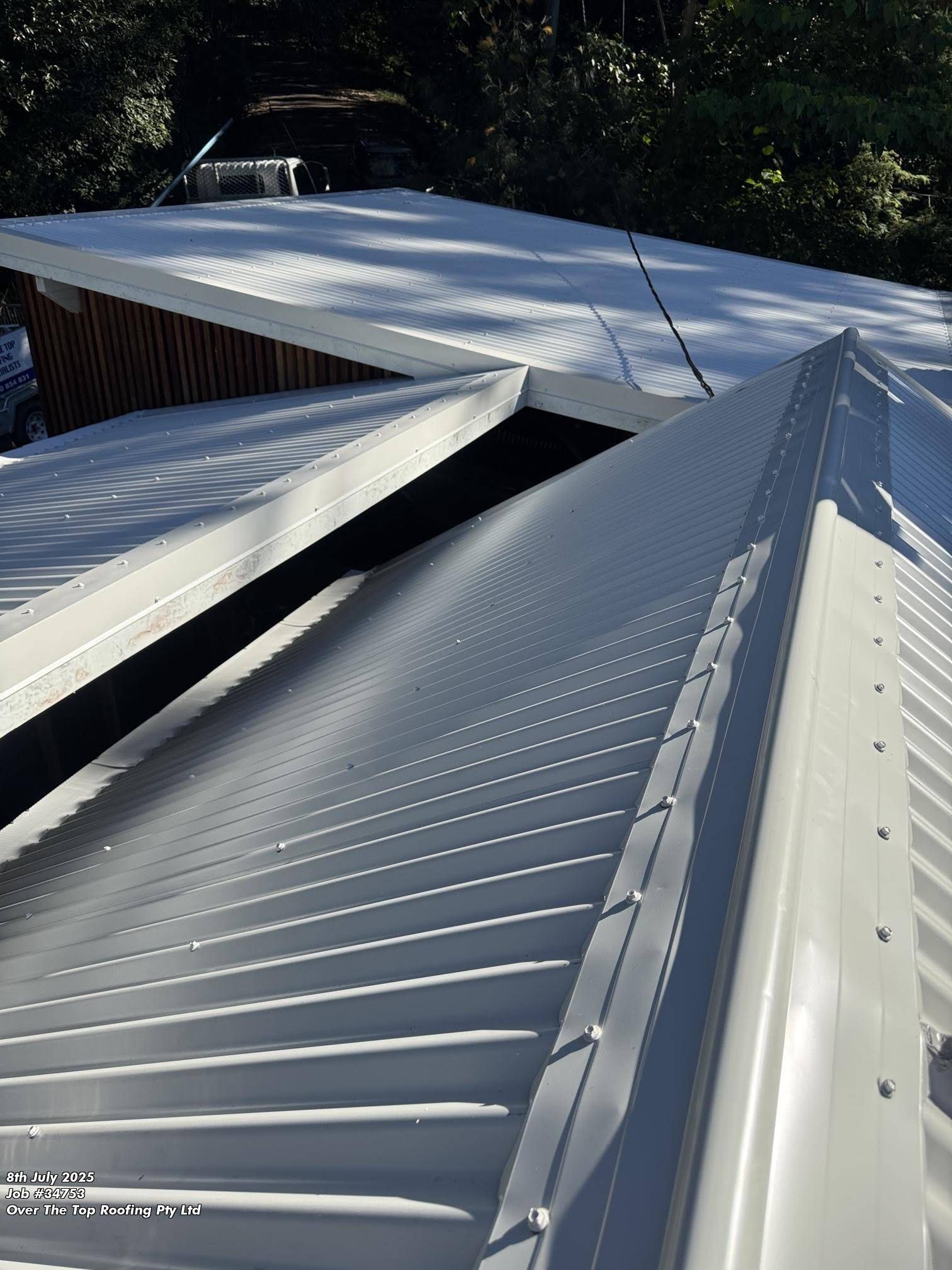 White Metal Roof With Ridged Panels Meeting at Angles, Sunny Setting — Over the Top Roofing Specialists in Gympie, QLD