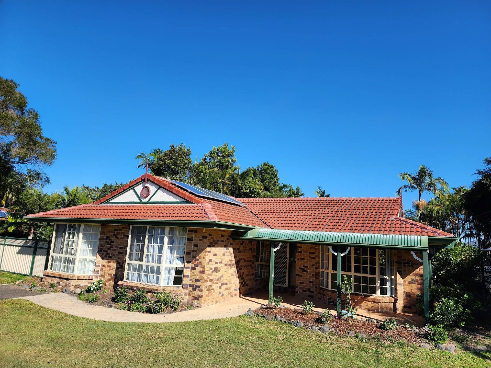 Brick House With Red-tile Roof, Solar Panels, and Green Awning — Over the Top Roofing Specialists in North Lakes, QLD