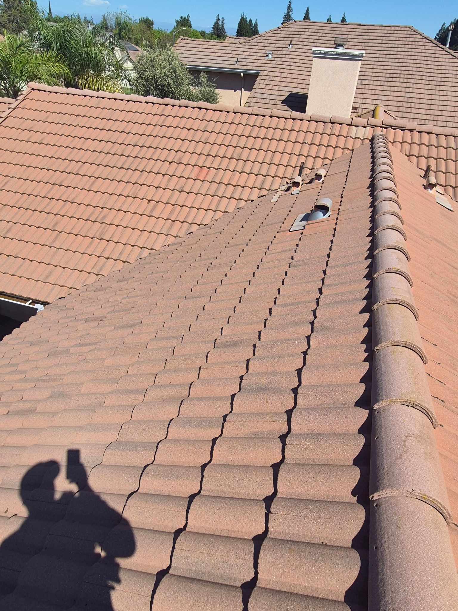 Sunlit terracotta tile roof with a roof vent and a person’s shadow in the foreground