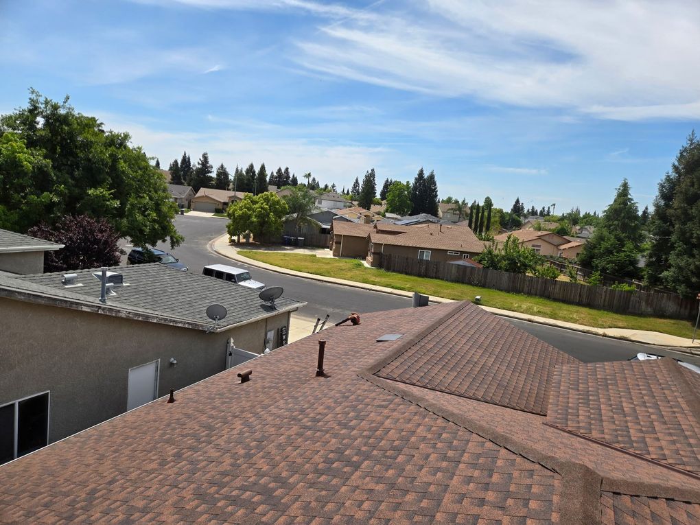 Suburban rooftops under a blue sky, with trees and houses in the background.